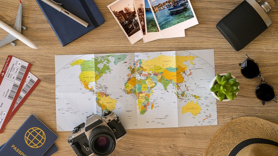 World map surrounded by holiday items like passport, sun glasses, camera and plane tickets
