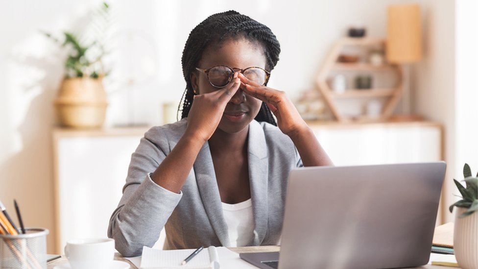 Woman at laptop looking stressed and rubbing her eyes under her glasses