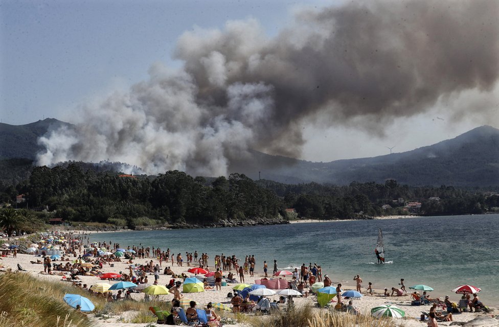 Smoke rises from a forest fire near a tourist beach