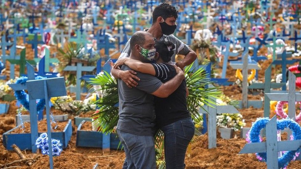 Three people hug at a cemetery