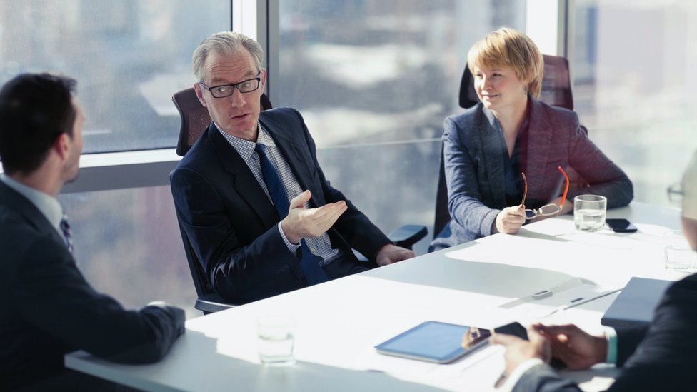 Korona virus i jednakost polova: Hoće li žene posle epidemije morati više da se trude na poslu 4 A company's board of directors, with two men talking and a woman looking on and smiling around a board table
