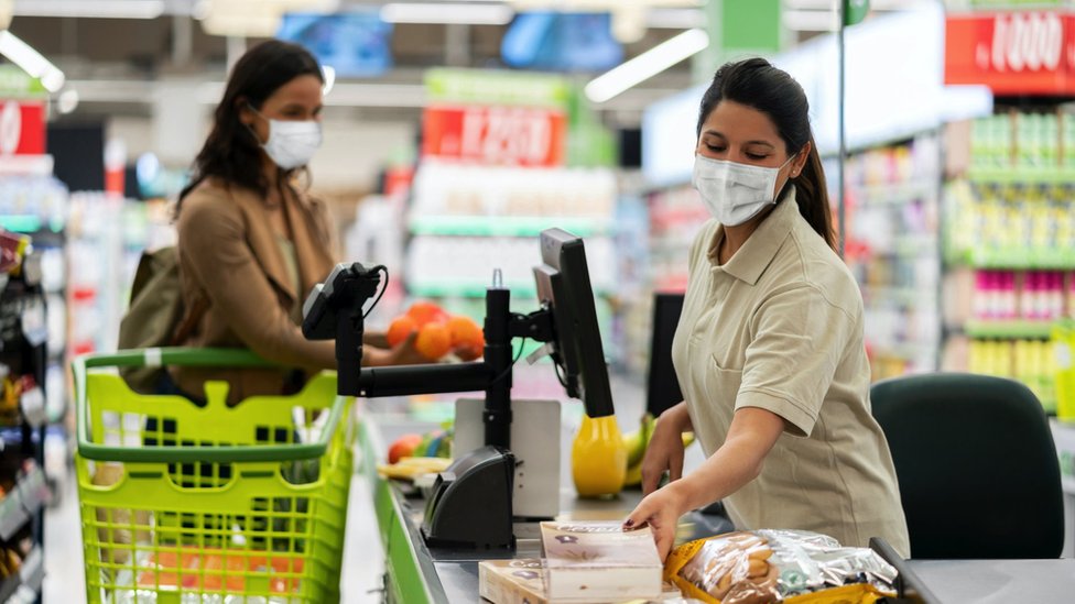 Korona virus i jednakost polova: Hoće li žene posle epidemije morati više da se trude na poslu 6 A woman shopping for food wears a face mask, as does the cashier