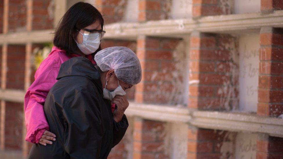 Korona virus nije pandemija već sindemija, kažu naučnici - šta to znači 1 Two women wearing face masks mourn at a cemetery in La Paz, Bolivia