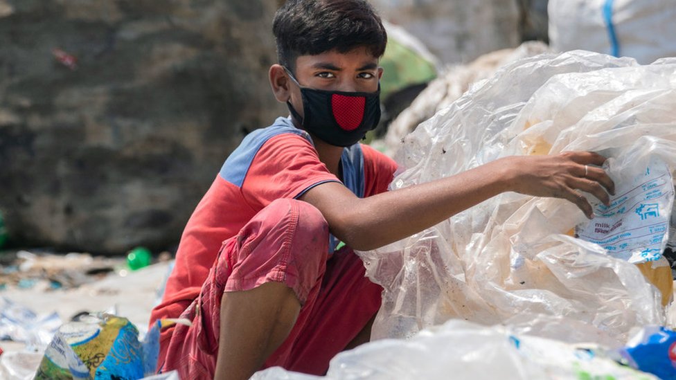A boy wearing a face mask rummages through garbage in Bangladesh