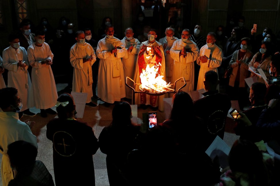 People gathered around a fire during a Mass in the Virgin Mary Church in Baghdad, Iraq. Photo: 24 December 2020