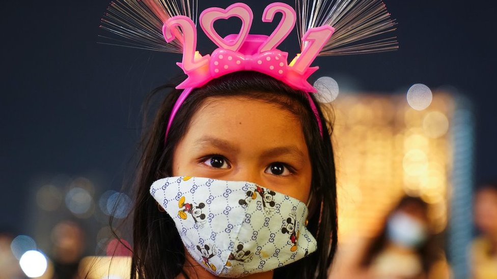 A young woman wearing a protective facce mask and "2021" head band looks on at a shopping mall as The New Year countdown celebrations in Bangkok
