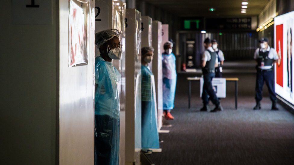 Health workers wearing protective gear wait for incoming travellers to arrive