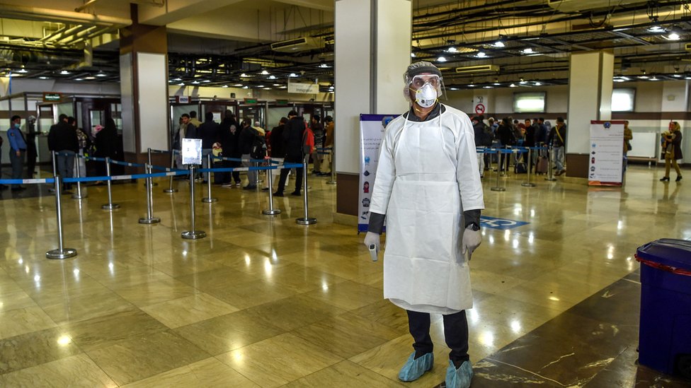A health services staff member wearing protective gear looks on as he waits to check