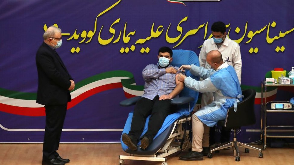 Iranian Health Minister Saeed Namaki (L) watches while his son Parsa receives the first Covid-19 vaccine