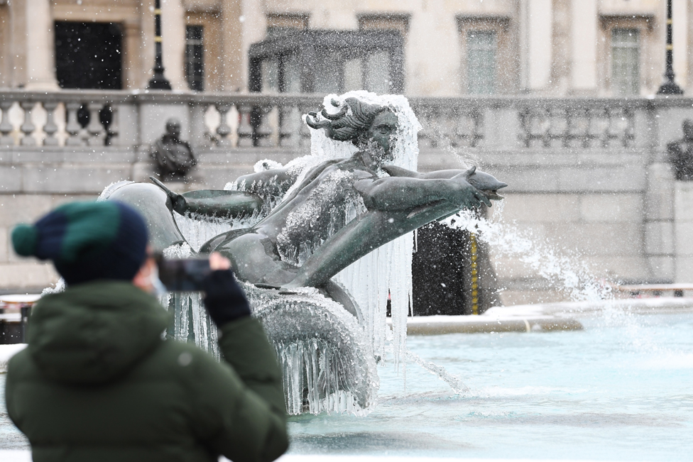 A man takes a photograph of an ice-covered mermaid statue in Trafalgar Square, London, on 9 February 2021