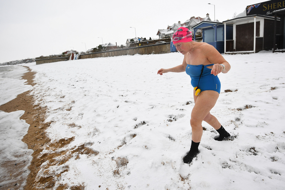 An early morning swimmer walks down a snow-covered beach at Thorpe Bay, Essex, on 9 February 2021