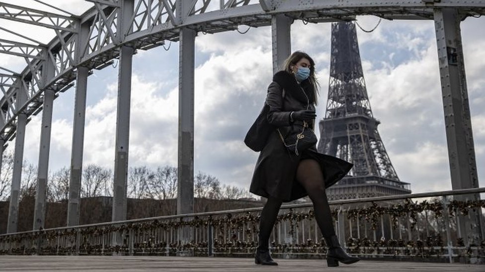 A woman wears a face mask as walks across a footbridge near the Eiffel Tower in Paris, France. Photo: 19 March 2021