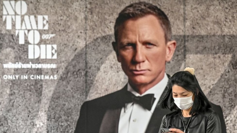 Korona virus i film: Kako Kovid-19 preti da spusti zavesu na „najstariji bioskop na svetu“ 2 A woman wearing a face mask looks at her phone while standing in front of the new James Bond movie