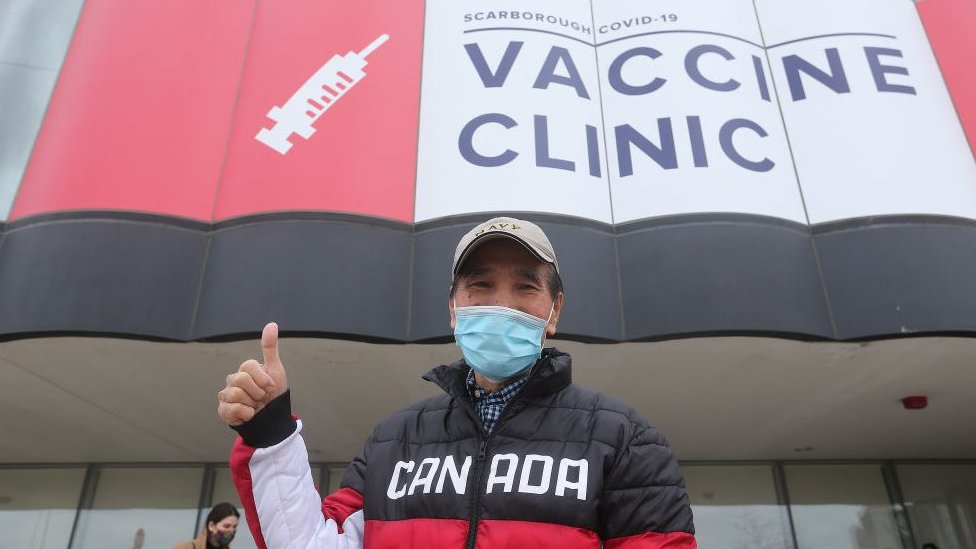 Korona virus: Kada će svet biti vakcinisan 5 A man in a Canada jacket showing thumbs up at a vaccine centre