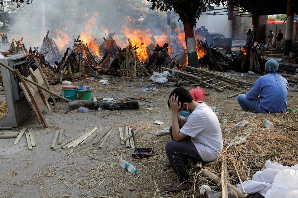 Family members sit next to the burning funeral pyres in New Delhi, India
