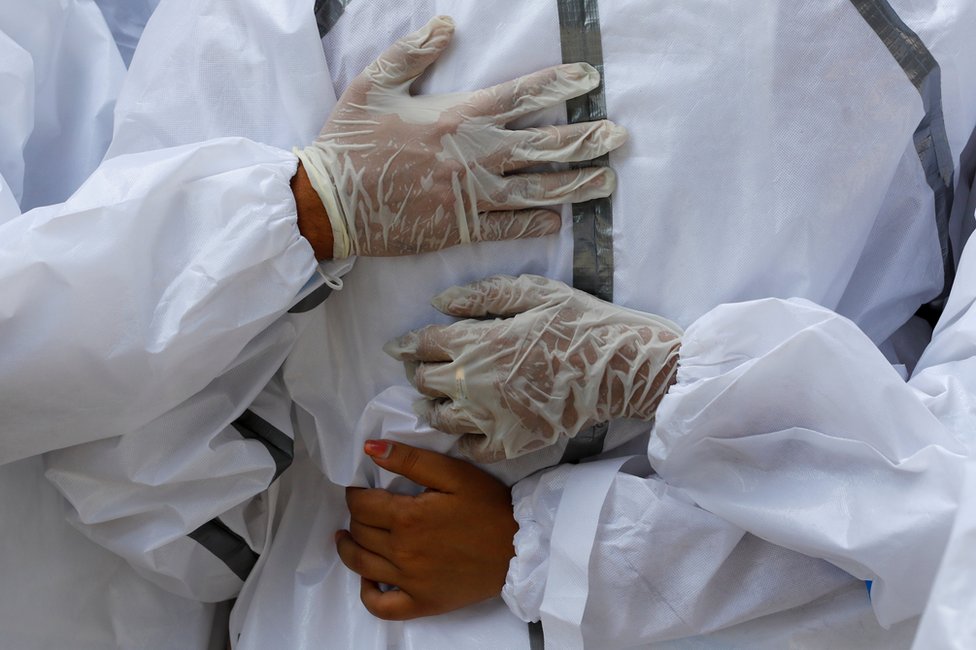 Relatives wearing personal protective equipment (PPE) mourn a man and place hands on each other's backs
