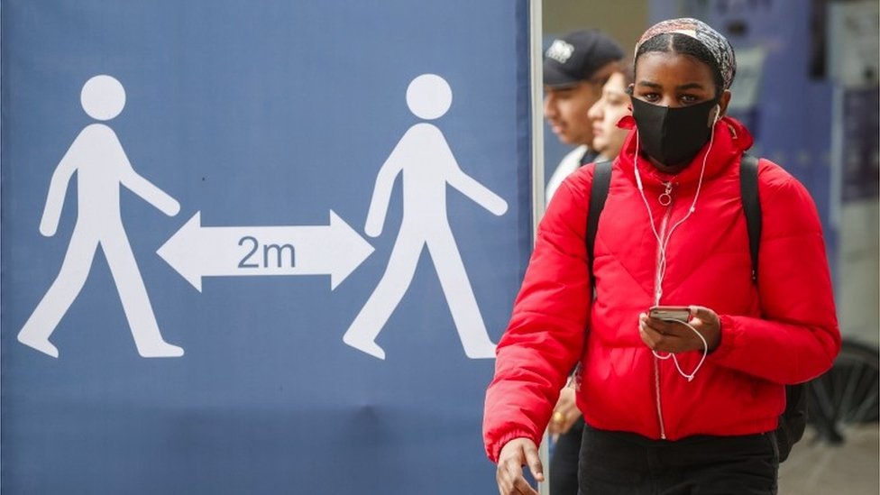 Kovid kriza u Velikoj Britaniji: Teške optužbe na račun premijera - „Umrle su desetine hiljada ljudi koje nisu morale da umru“ 4 A woman walks past a sign calling for social distancing
