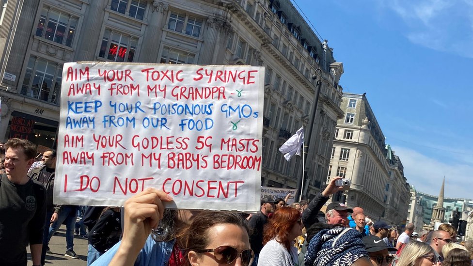 Korona virus, teorije zavere i društvene mreže: Dobrovoljci koriste „mamac“ grupe za borbu protiv antivakcinalne propagande 3 Woman with a sign listing conspiracy theories about toxic syringes and 5G phone technology