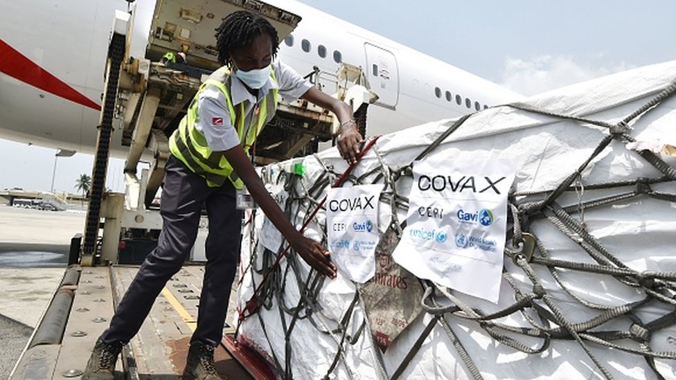 A woman puts on Covax stickers as workers unload a shipment of AstraZeneca Covid-19 vaccines
