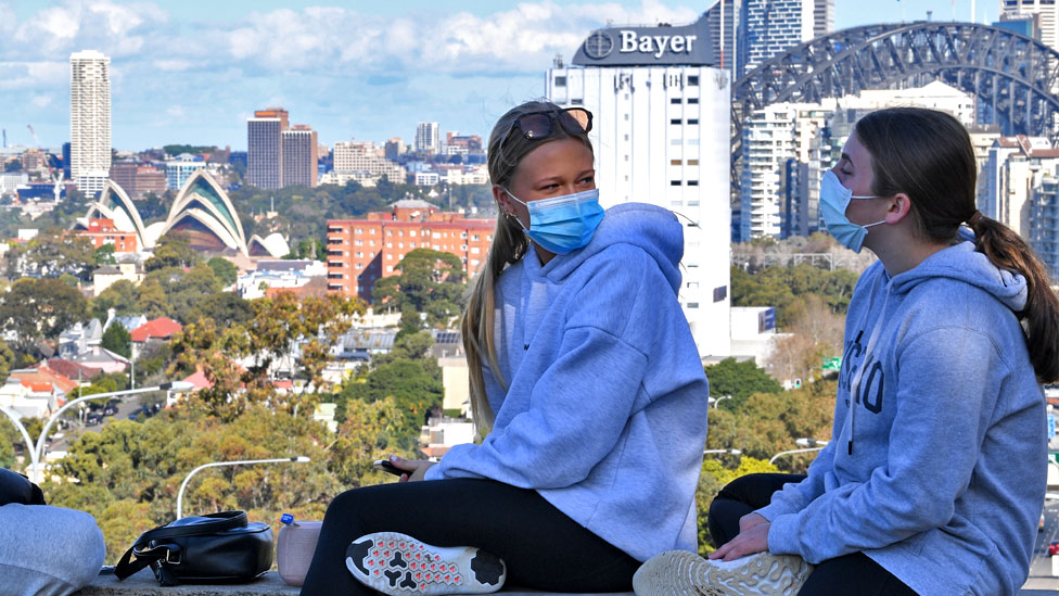 Korona virus: „Ljudi u Srbiji su neposlušni", kažu stručnjaci, naučnici analiziraju da li je potrebna treća doza vakcina 1 Two girls wearing face masks sit above the Bradfield Highway in the suburb of North Sydney with the city in the background on July 07, 2021 in Sydney, Australia.