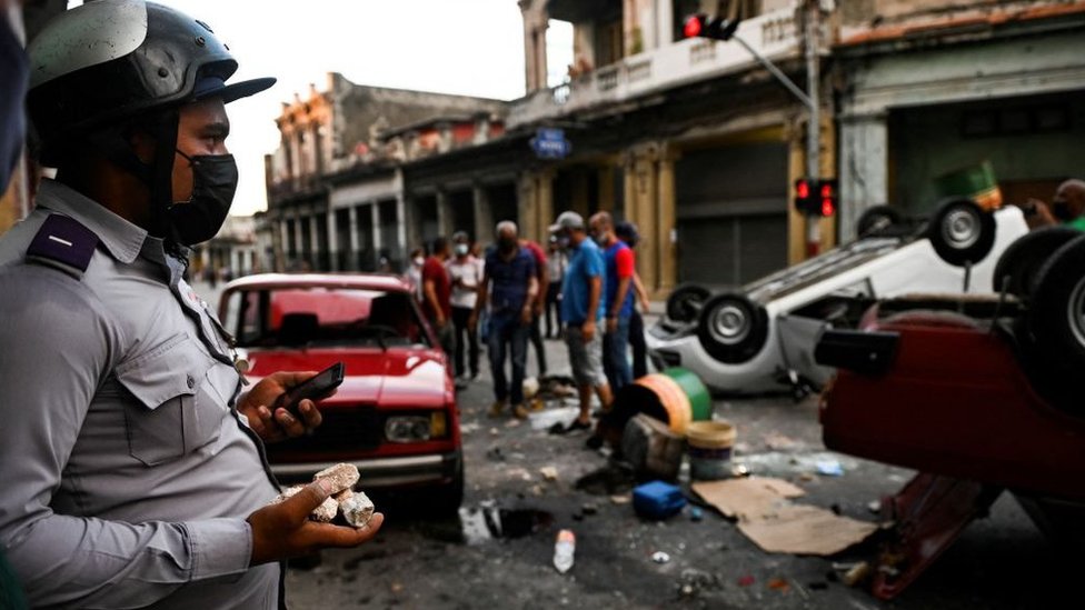 Police officer stands by as protesters overturn police vehicle, Cuba (11 July)