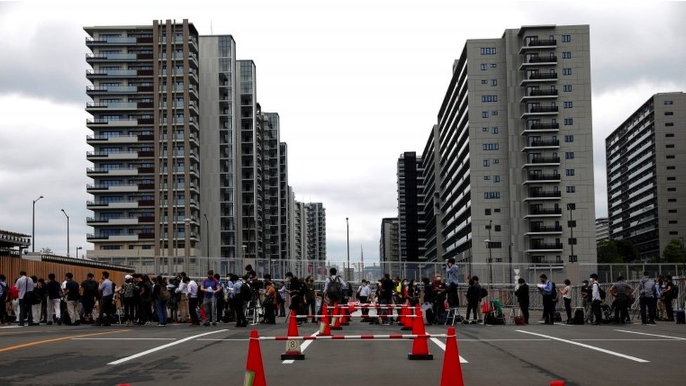 Fences and people queue outside the Olympic Village