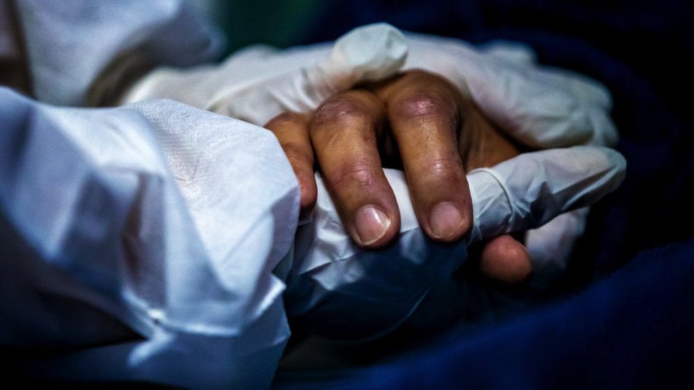 A health worker wearing personal protective equipment (PPE) holds the had of a patient at on 30 April 2021at a hospital in Maricá, Brazil.