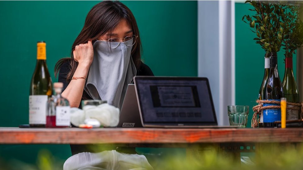 A woman wearing a mask for protection works on her computer in a restaurant in Shanghai, China, 21 August 2021.