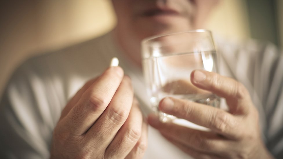 Korona virus i najčešća pitanja: Sve što ste hteli da znate o Kovidu-19 9 A woman holds a painkiller pill and a glass of water