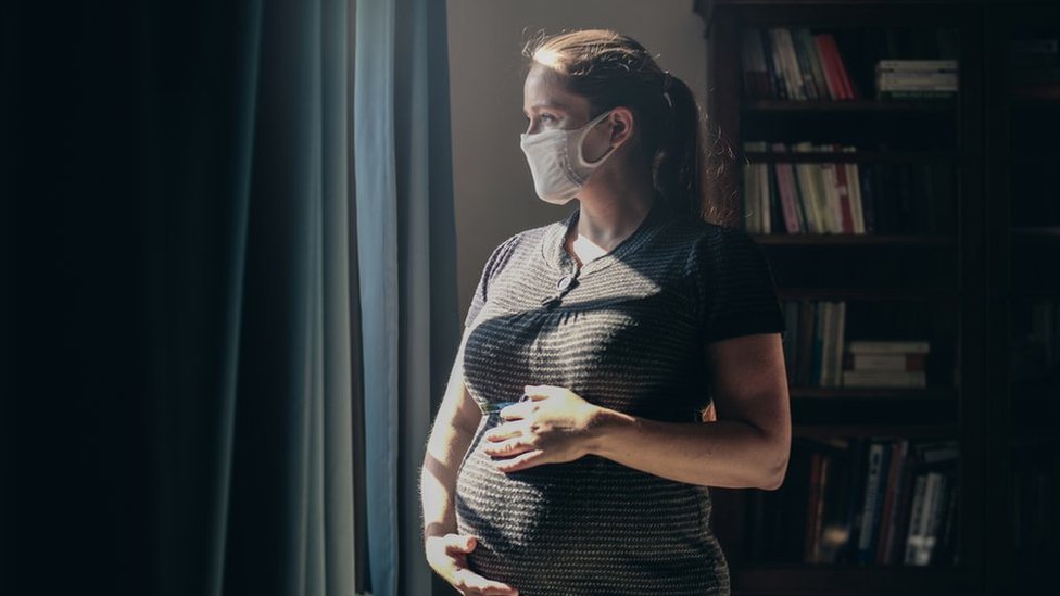 Picture of pregnant lady with mask looking out of window