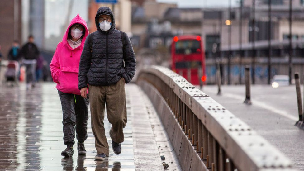 Two people walking in London wearing masks