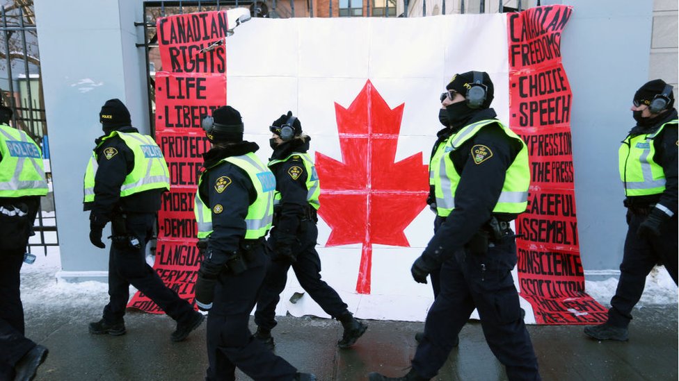 Korona virus i Kanada: Ni posle skoro dve nedelje ne nazire se kraj proitestima, policija preti hapšenjima 5 A group of police officers walk past a Canadian flag near Parliament Hill