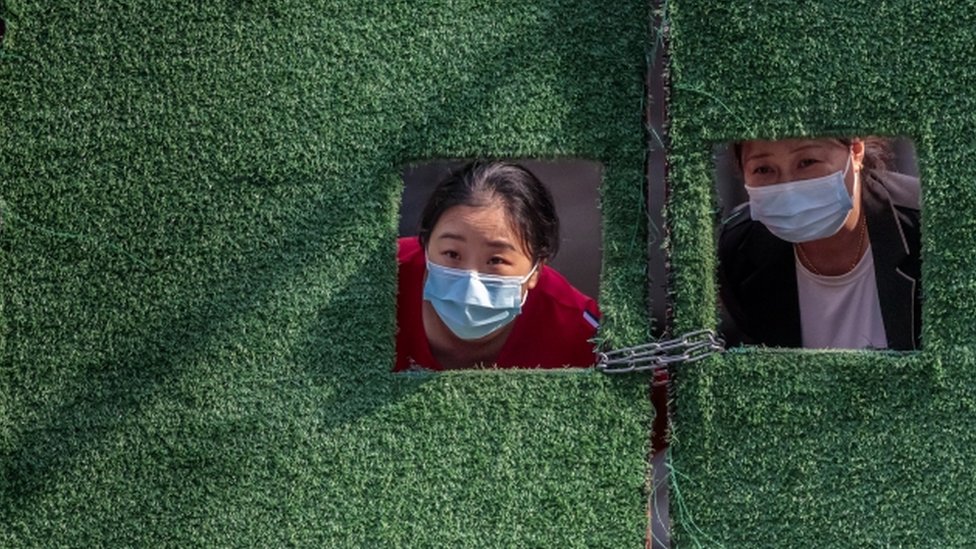 Kina i korona virus: Kako će izmučeni Šangaj konačno izaći iz karantina 1 Women in quarantine look through small windows in a green fence, amid the Covid-19 lockdown in Shanghai, on 2 May 2022