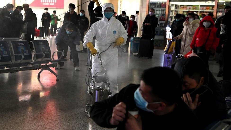 Putnici reaguju dok radnik u zaštitnom odelu dezinfikuje zonu polaska železničke stanice u Hefeju, kineska istočna provincija Anhui, 4. marta 2020.